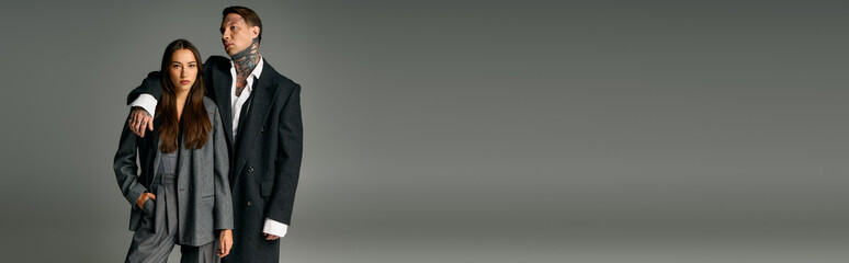 A young attractive couple stands together exuding confidence with modern attire and striking looks.