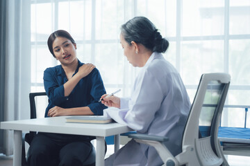 Doctor Patient Consultation:  A young woman describes her shoulder pain to a senior female doctor during a consultation in a bright, modern office.  The image conveys care.