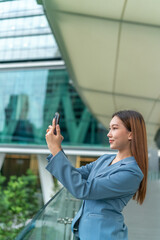 Obraz premium Young Businesswoman In Blue Suit Using Phone Outdoor In Front A Modern Office Building In A Business Financial District