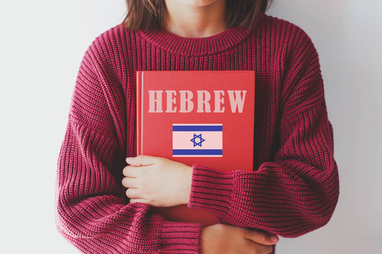 one girl schoolgirl in burgundy sweater holds red ivrit language textbook with Israel flag. foreign language learning concept