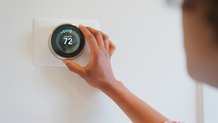 Close Up Of Woman Setting Digital Smart Heating Thermostat At Home