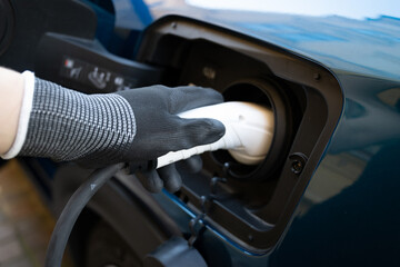 Electric car charger plugged in a blue car and a hand on globes holding it. Close up picture