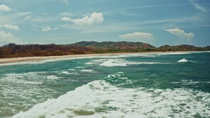 Flying low over the long stretching beach in Nosara, Costa Rica. View of the big waves coming to the shore. Destination of surfers and water sports enthusiasts.