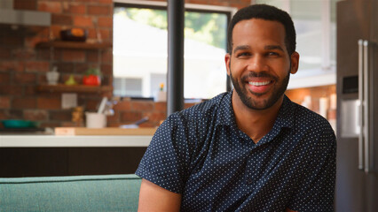 Portrait Of Smiling Young Man Relaxing On Sofa At Home