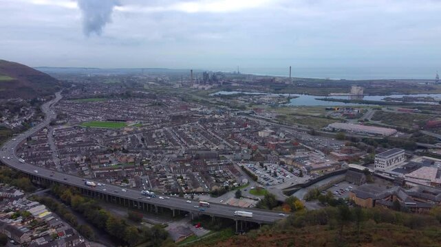 Pushing Aerial Shot of M4 Motorway with Traffic Flowing with Cars, Vans, Trucks with Rows of Houses with Steelworks and Industrial Landscape in Background with Ocean 4K