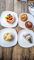 Top view of Plates desserts that include cake slices, tarts and pavlova on a wooden table