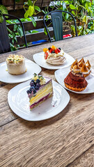 Plates desserts that include cake slices, tarts and pavlova on a wooden table in the garden