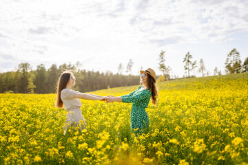 Fototapeta premium Two beautiful women in amazing in a blooming field. Nature, vacation, relax and lifestyle. Summer landscape.