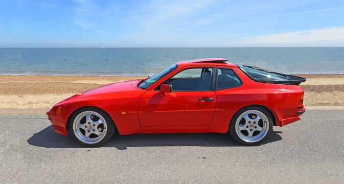 Classic Red Porsche 944 Turbo Coup&eacute; parked on seafront promenade beach and sea in background