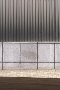 A contemporary architectural design featuring a sleek corrugated metal cladding above smooth stone wall panels, providing an urban minimalist aesthetic.