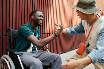 Side view portrait of smiling African American man with disability greeting friend with handshake...