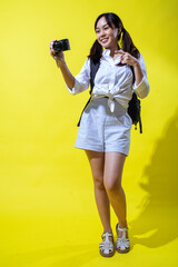 An Asian woman in a white shirt and striped shorts, holding a camera while enthusiastically...