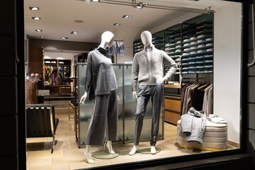 Female and male mannequins in store glass window display dressed casual autumn — winter elegant clothing, night scene