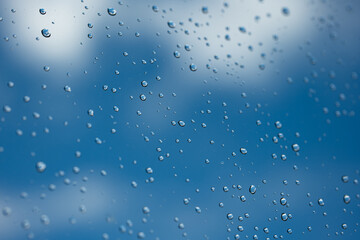 Water droplets on glass window. Blue sky and white clouds in the background, close up macro shot