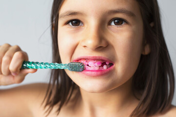 close-up portrait of 7 year old girl brushing teeth with toothbrush after applying pink solution to indicate plaque detection, concept of dental hygiene and health