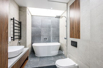 Modern bathroom with gray tile, a freestanding white bathtub, and a sleek, minimalist design. ...