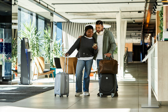 A young couple joyfully arrives at a modern hotel lobby, eager to start their vacation filled with adventure.