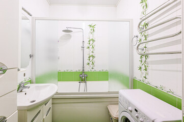 bathroom features a white bathtub/shower combo with frosted glass doors, green tile accents, and a...