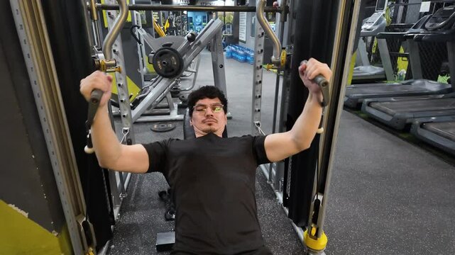 Handsome, Well-Toned Man Wearing Glasses Performing Cable Incline Fly for Chest Development, Demonstrating Fitness Dedication on an Incline Bench with Cable Fly Machine in Gym Workout