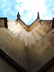 Obraz premium Architectural photograph showing the corner of an ancient Gothic-style building, taken from the bottom up. Stonework, texture and grandeur of architectural heritage, blue sky with clouds, majesty
