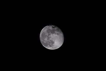 The moon in the night sky with a silhouette of an airplane. The moon in the dark sky with a plane flying over it.