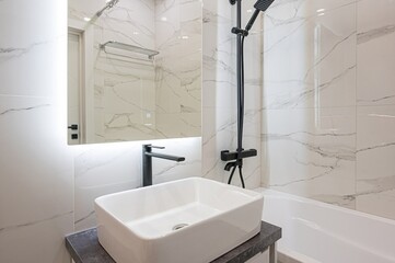 interior apartment minimalist bathroom with white marble tiles, black fixtures, a sleek bathtub,...