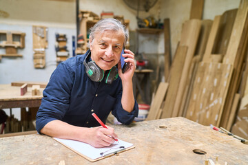 Experienced carpenter working in workshop while communicating on phone