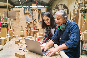 Experienced mentor and apprentice collaborate in a busy lumber workshop