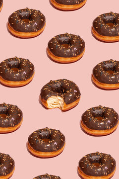 Pattern of chocolate donuts with sprinkles and a single bite