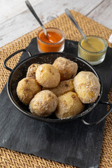 A rustic black dish of papas arrugadas, a traditional Canarian dish, elegantly arranged and garnished with coarse salt, served with vibrant red and green sauces.