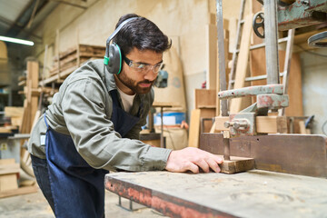 Focused young worker using a saw in a lumberyard workshop