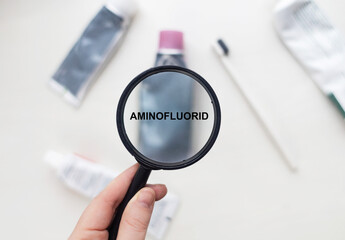 Aminofluorides in natural toothpaste. Magnifying glass is directed at a tube with a list of ingredients of a safe product. Safe toothpaste composition