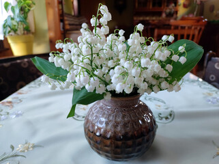 bouquet of blooming lily of the valley in the clay vase at the table