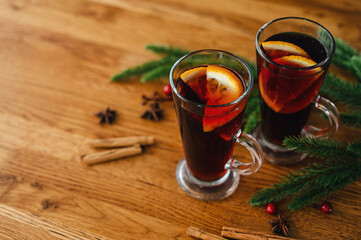 Two glasses of christmas mulled wine with oranges and spices on wooden background