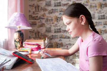 Teenage girl sitting at table in room writing homework in notebook