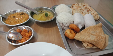 An Asian-style platter of string hoppers, pittas, ulunthu vadai, and parathas. They are accompanied by a well-seasoned lentil curry, a potato stew, and a red coconut sambol. Indian style Street food