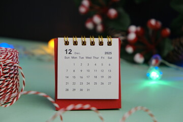 Monthly desk calendar for December 2024 year on wooden table with black alarm clock.