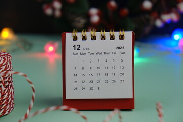 Monthly desk calendar for December 2024 year on wooden table with black alarm clock.