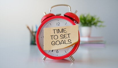 TIME TO SET GOALS is written on sticker and near red alarm clock on light background.