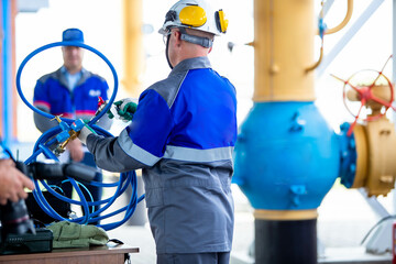 In the photo, a factory worker in a blue suit and a white helmet on his head. He works with his hands at a factory or large enterprise, his back turned