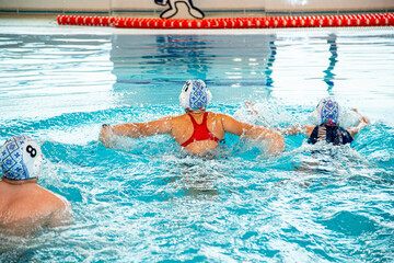 На фотографии изображены дети которые тренируются водным поло в большом и светлом бассейне.