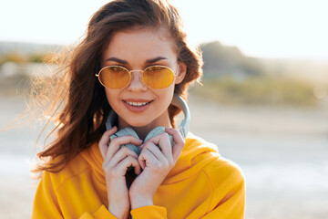 Fashionable woman in sunglasses and yellow sweater holding earbuds