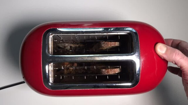 A man makes toast in a red toaster in a domestic kitchen. 