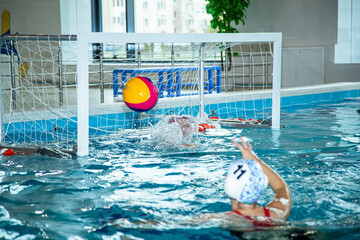 The photo shows children practicing water polo in a large, bright pool.