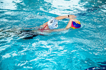 На фотографии изображены  как дети которые тренируются водным поло в большом и светлом бассейне.