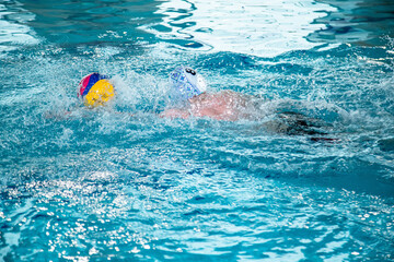 The photo shows children practicing water polo in a large, bright pool with lots of water.