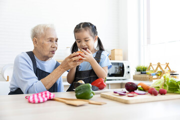 cute asian little child girl holding bell pepper with grandmother in the kitchen