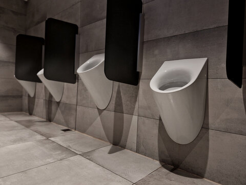 toilets separated by glass partitions. light tiled room. some men may have problems with being ashamed in front of others. therefore they cannot urinate together.