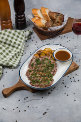 Grilled steak with chimichurri, roasted potatoes, and rich gravy, served on a white plate. Complemented by a breadbasket, red wine, and a cozy table setting