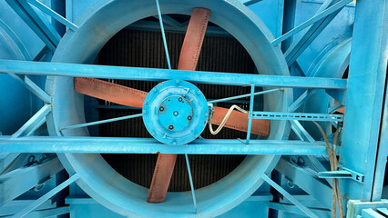 На фотографии современный вентилятор синего цвета с желтым цветом детали на нем  для охлаждения оборудование на открытом воздухе